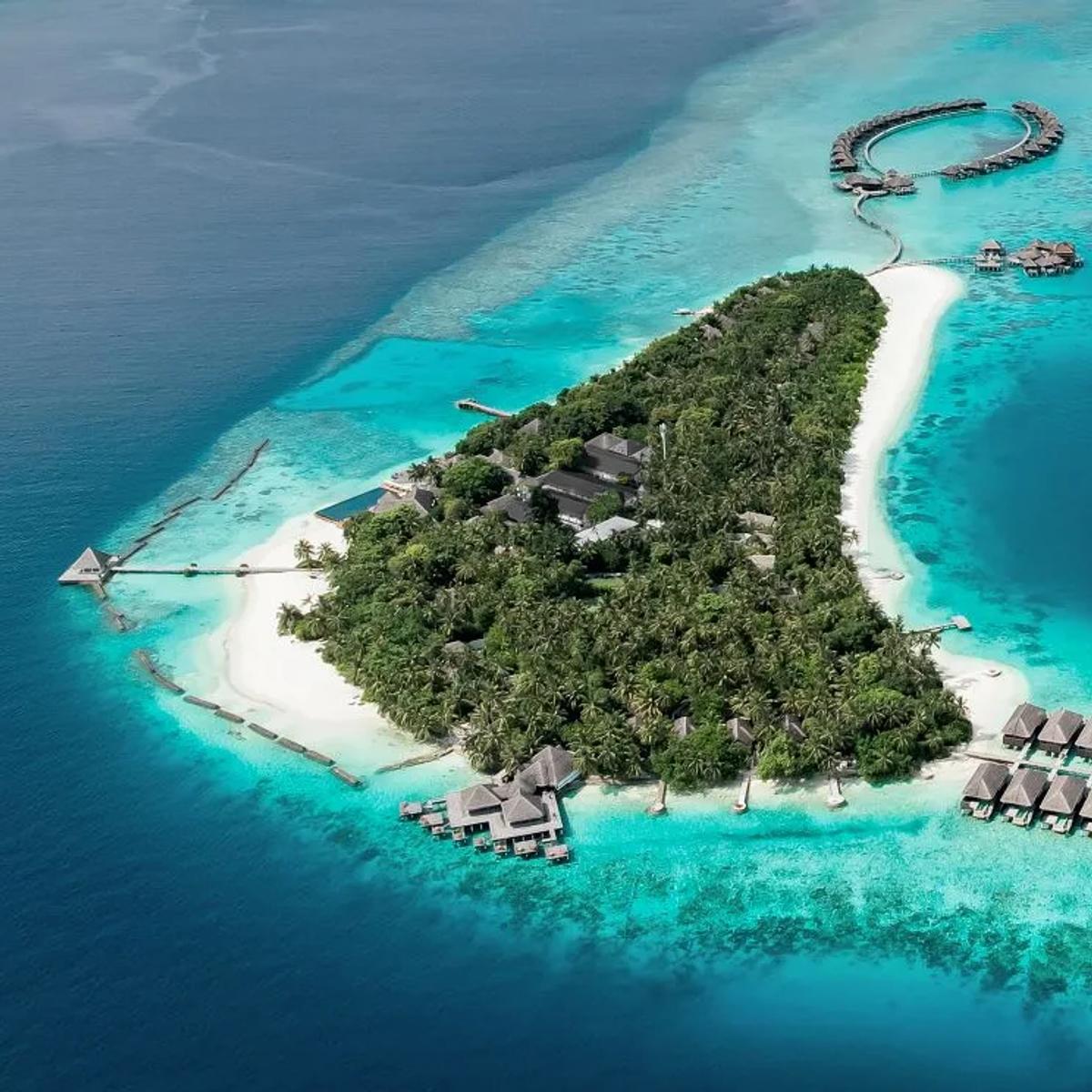 Aerial view of Coco Bodu Hithi's ring-shaped overwater villa cluster and second row of water villas curving into the North Malé Atoll lagoon