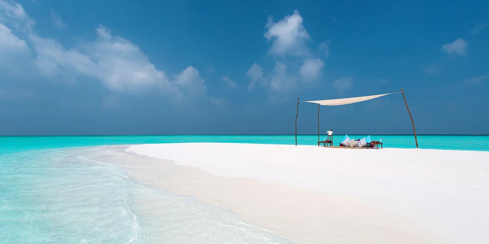 A shaded canopy set up on a sandbank near Milaidhoo, with cushions and a table laid for two.