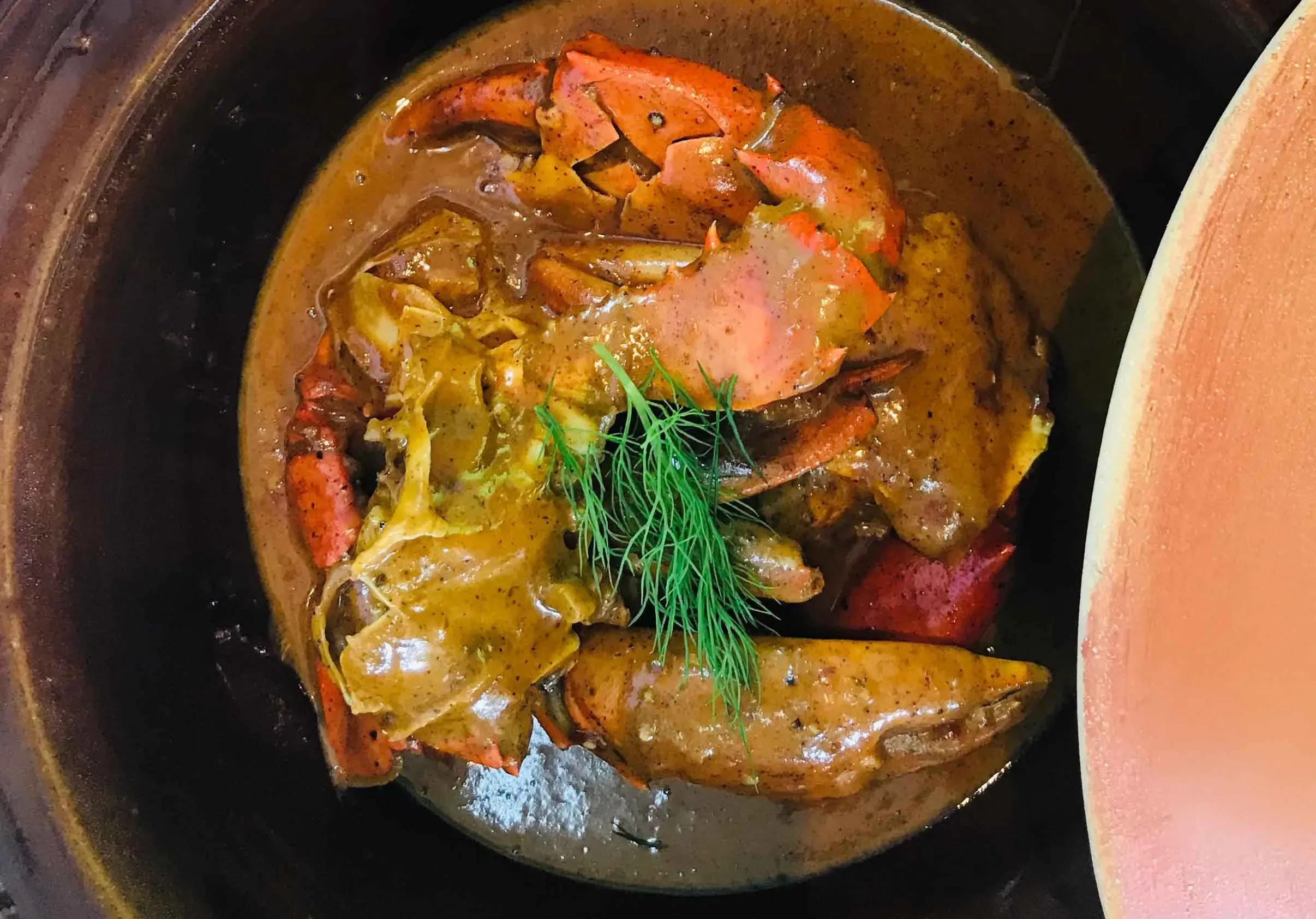 Crab Shack's mud crab curry, plated in a dark clay pot and garnished with dill, shot from above