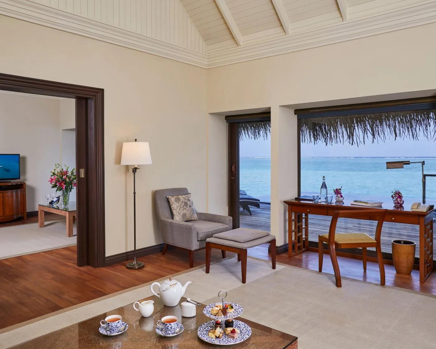 A One Bedroom Sunrise Overwater Suite's living room, afternoon tea set on the table beside a desk looking over the lagoon