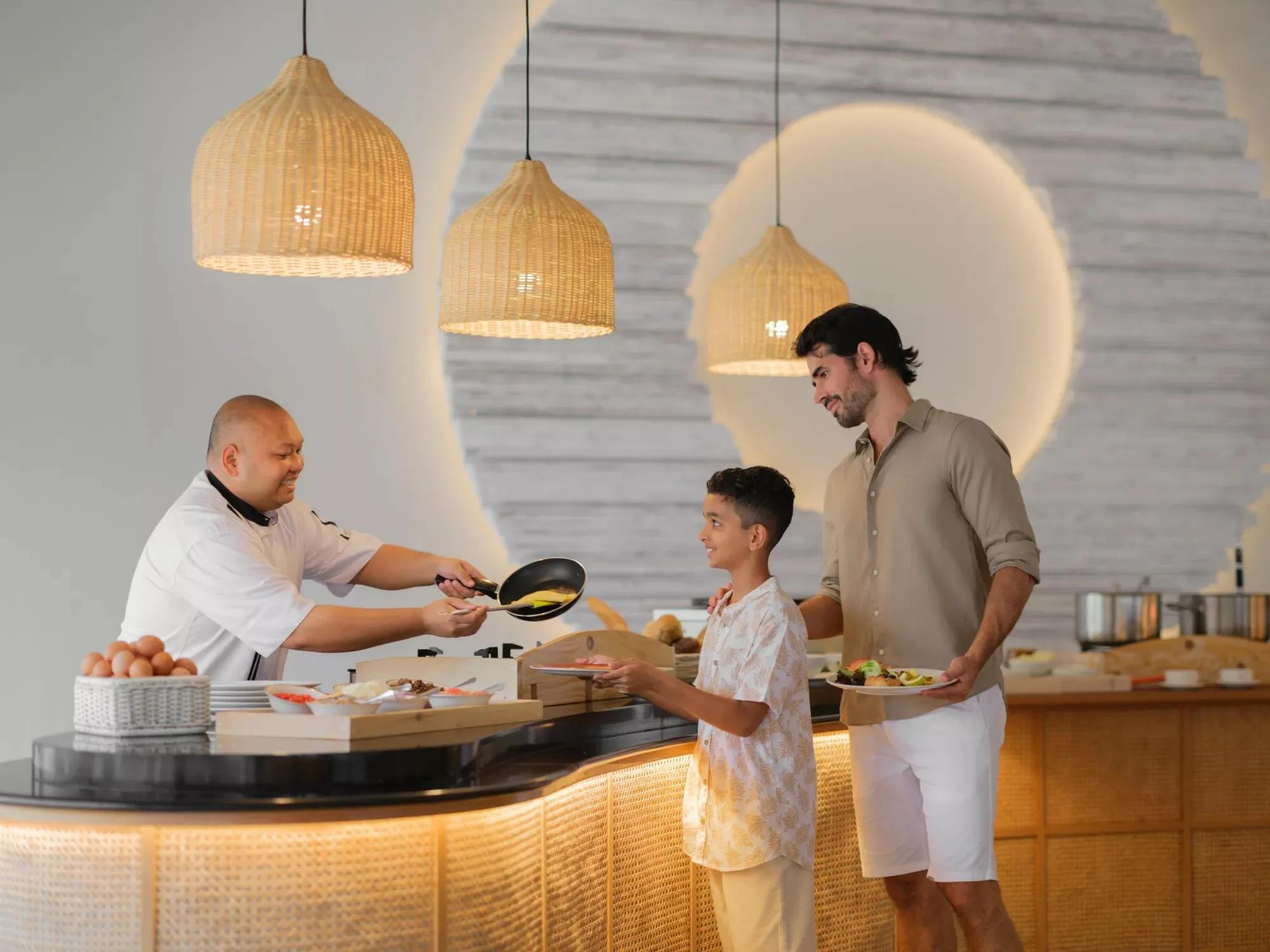 A chef serves a father and son from the live cooking station at Palms Restaurant, Noku Maldives