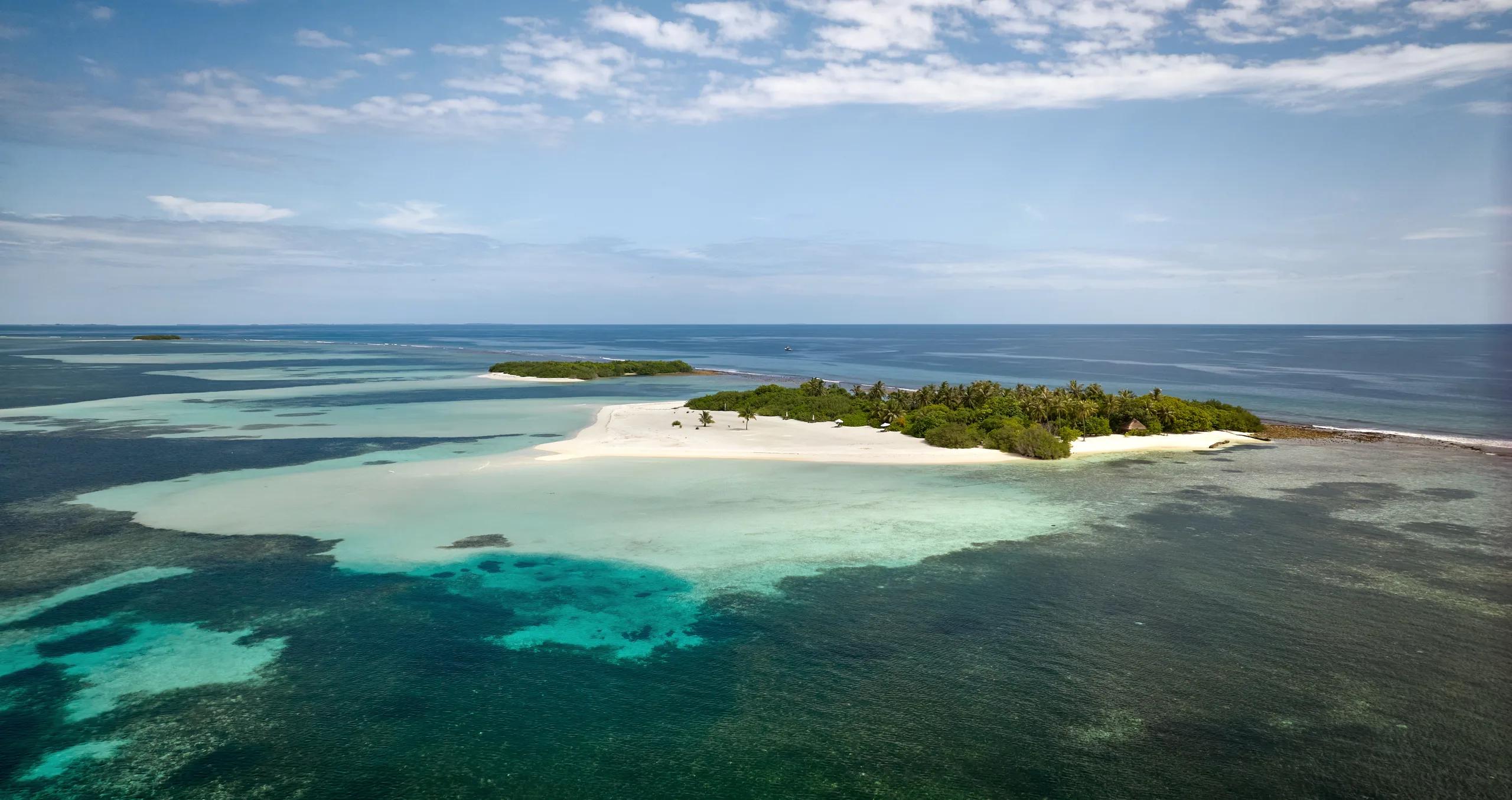 Aerial view of Jehunuhura, a narrow sandy islet with palm trees, surrounded by shallow turquoise water and reef.