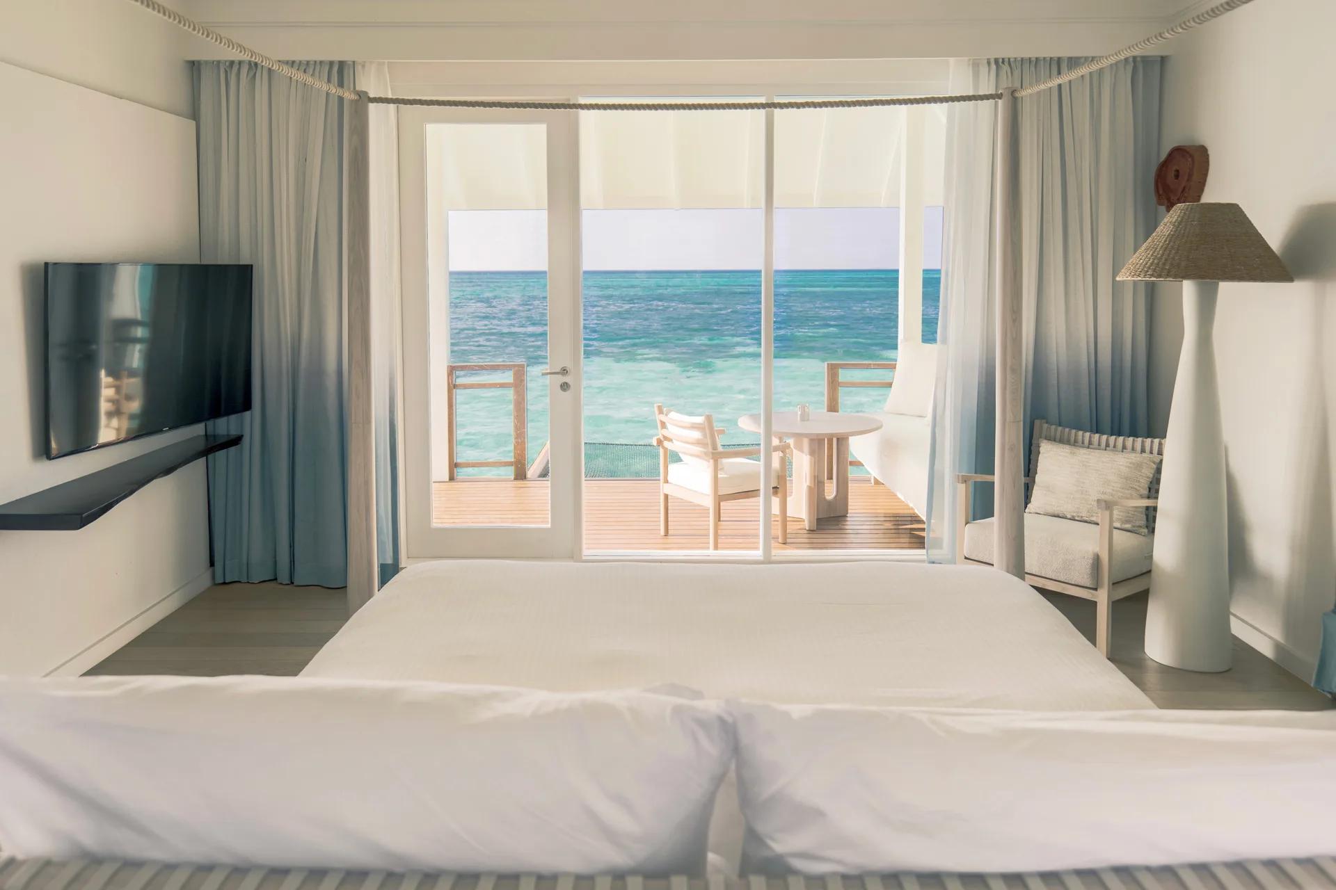 Interior of a Water Villa, its glass doors open to a deck set directly above the lagoon