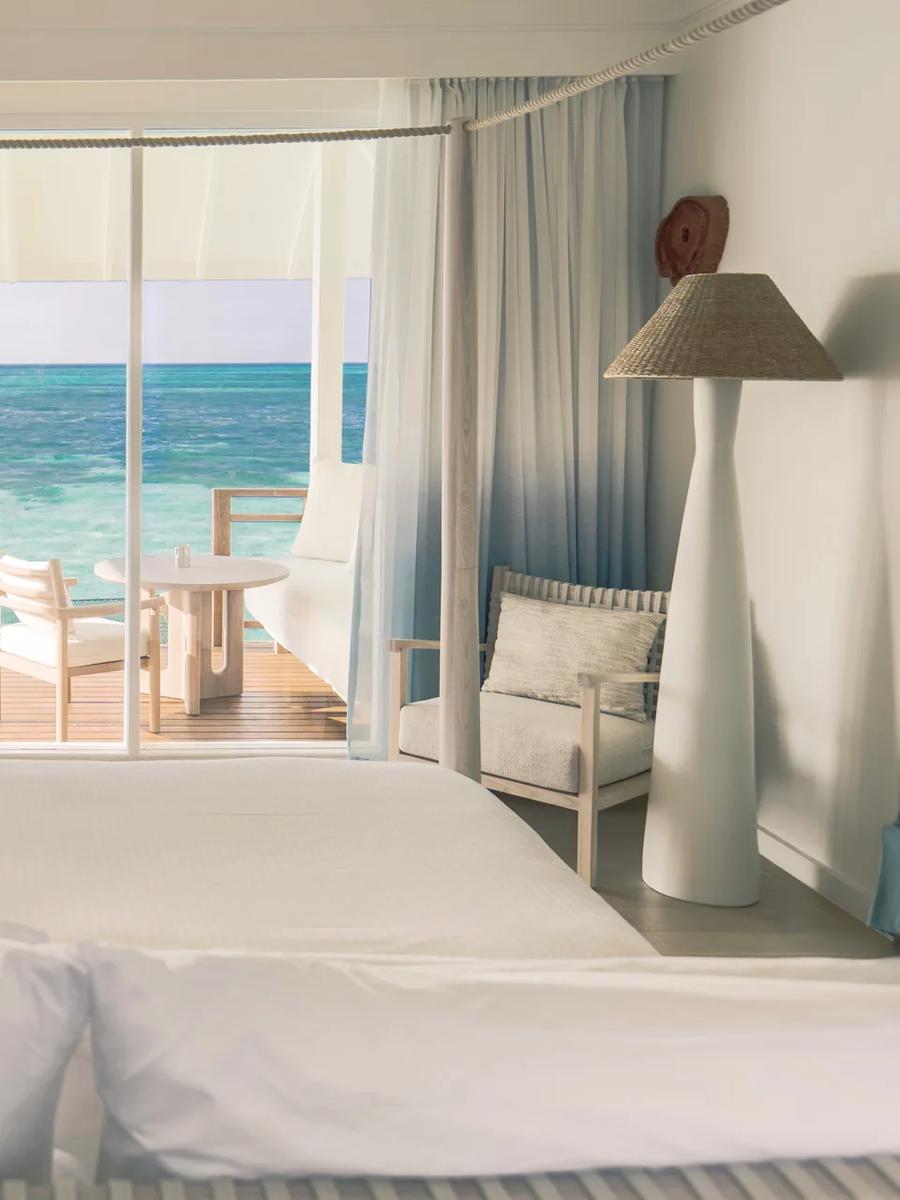 Interior of a Water Villa, its glass doors open to a deck set directly above the lagoon