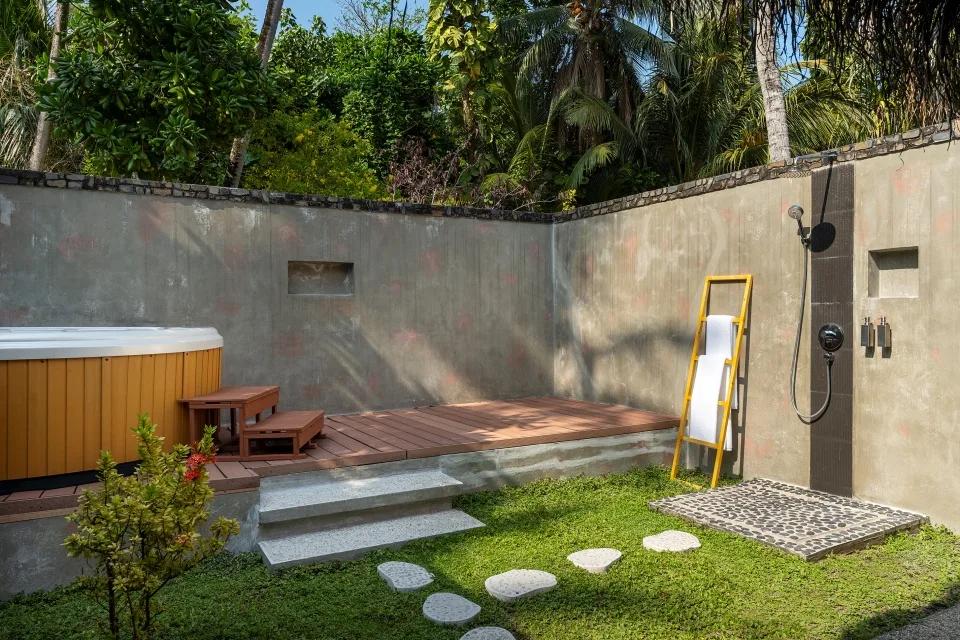 A Beach Bungalow's private garden bathroom, with an outdoor jacuzzi tub and a stone-tiled open-air rain shower screened by palms