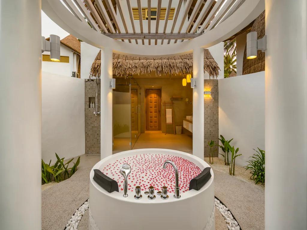 The open-air bathroom of a Premium Beach Villa at Bandos, with a jetted tub set beneath a circular skylight open to the palms