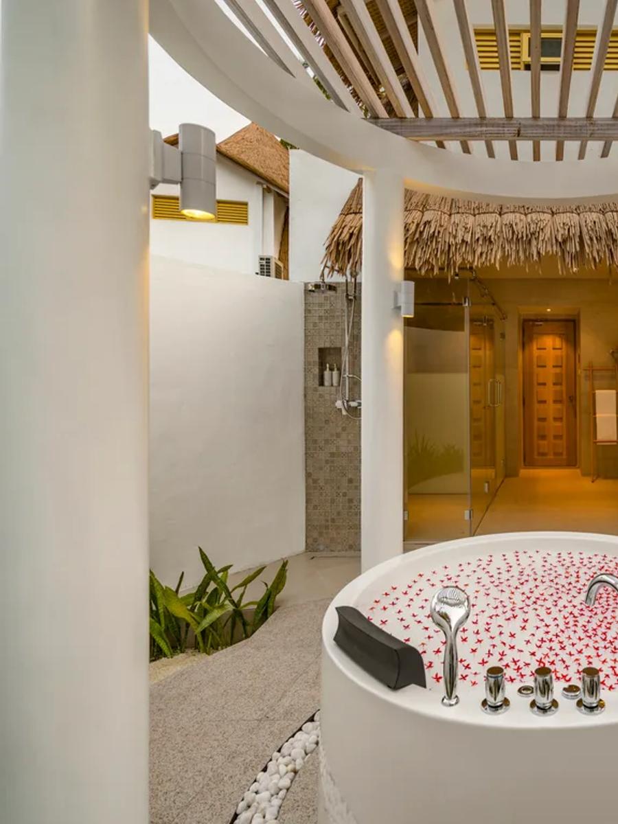 The open-air bathroom of a Premium Beach Villa at Bandos, with a jetted tub set beneath a circular skylight open to the palms