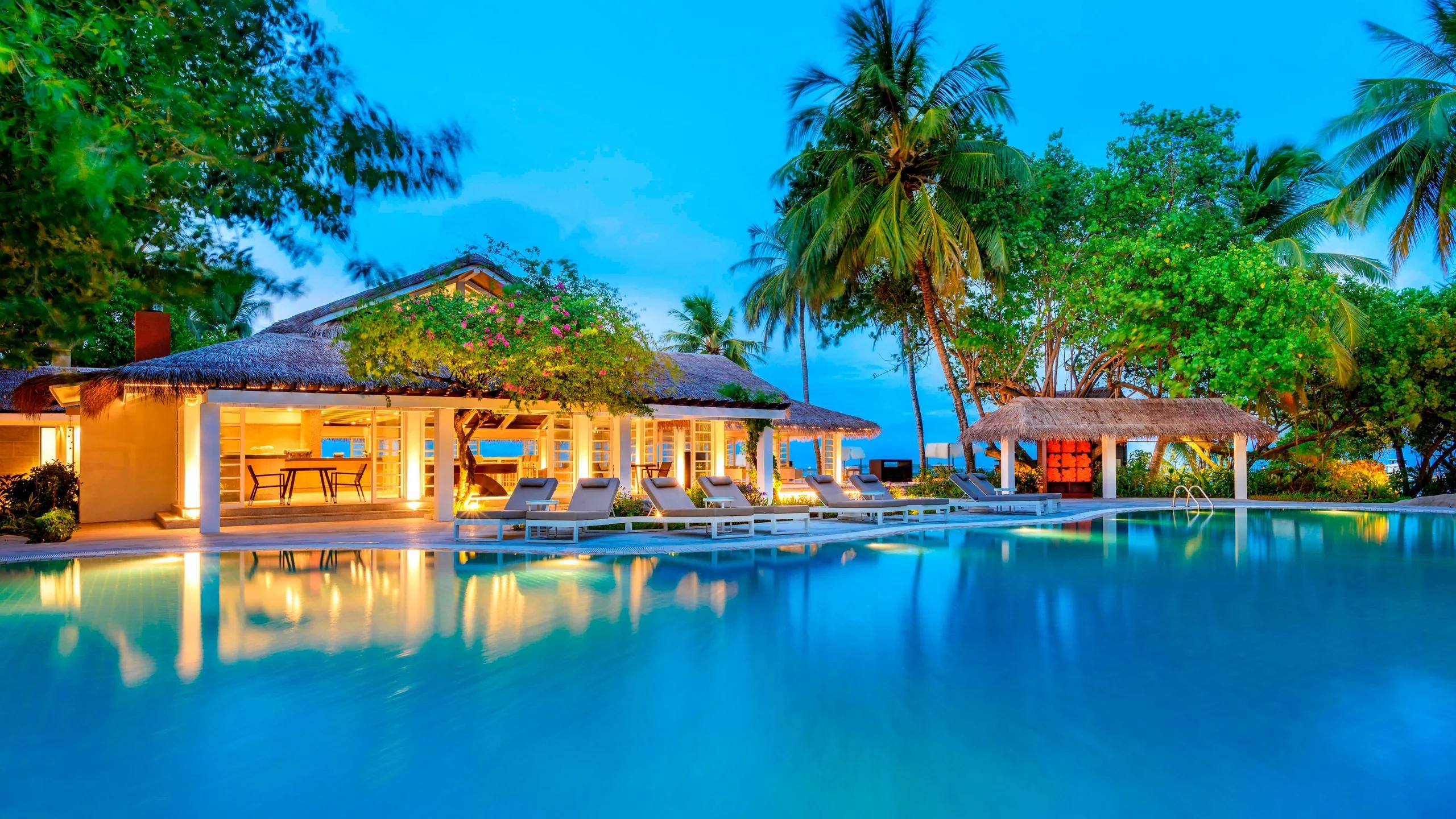 The resort's main pool at dusk, with loungers and a lit poolside pavilion reflected in the water