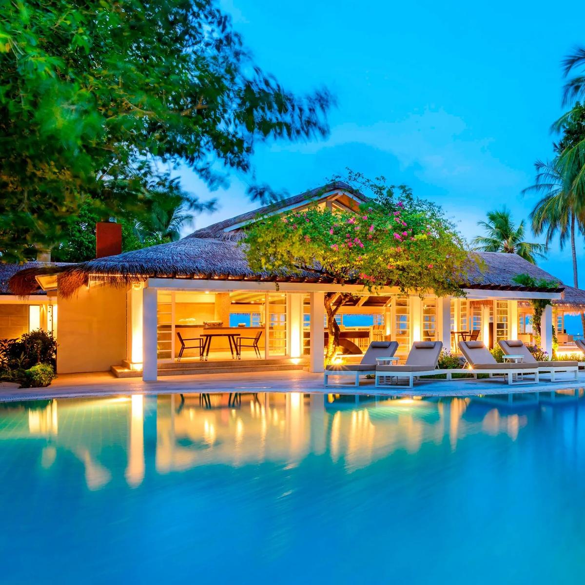 The resort's main pool at dusk, with loungers and a lit poolside pavilion reflected in the water