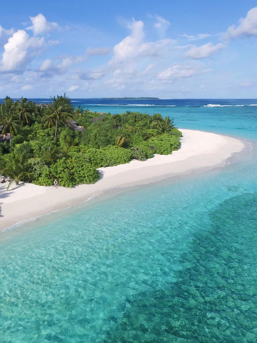 An elevated view over palm canopy toward a beach and turquoise lagoon, representative of the resort's two-bedroom beach villas