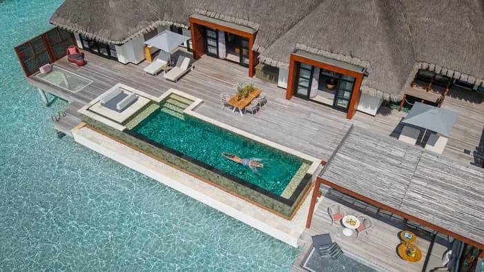 An elevated view over an overwater villa's plunge pool and thatched roof, the lagoon reaching to the horizon beyond