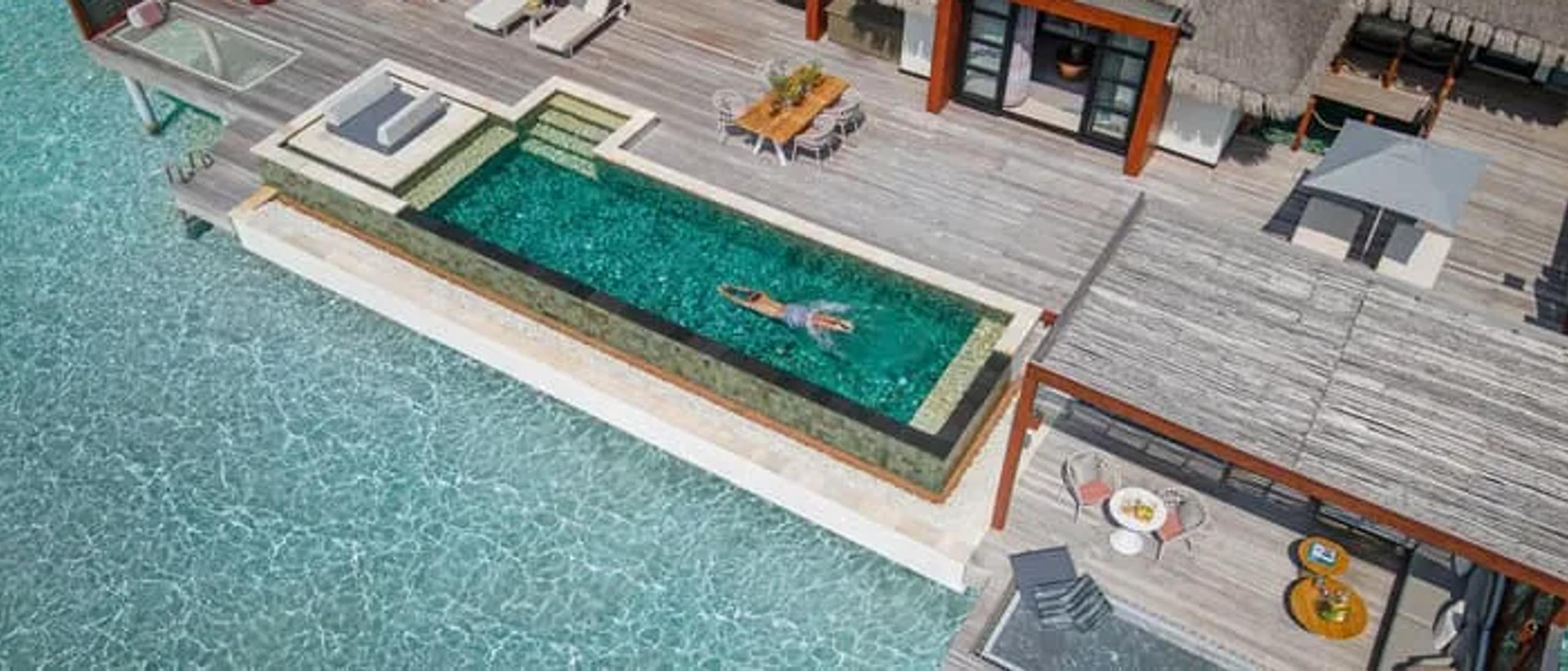 An elevated view over an overwater villa's plunge pool and thatched roof, the lagoon reaching to the horizon beyond