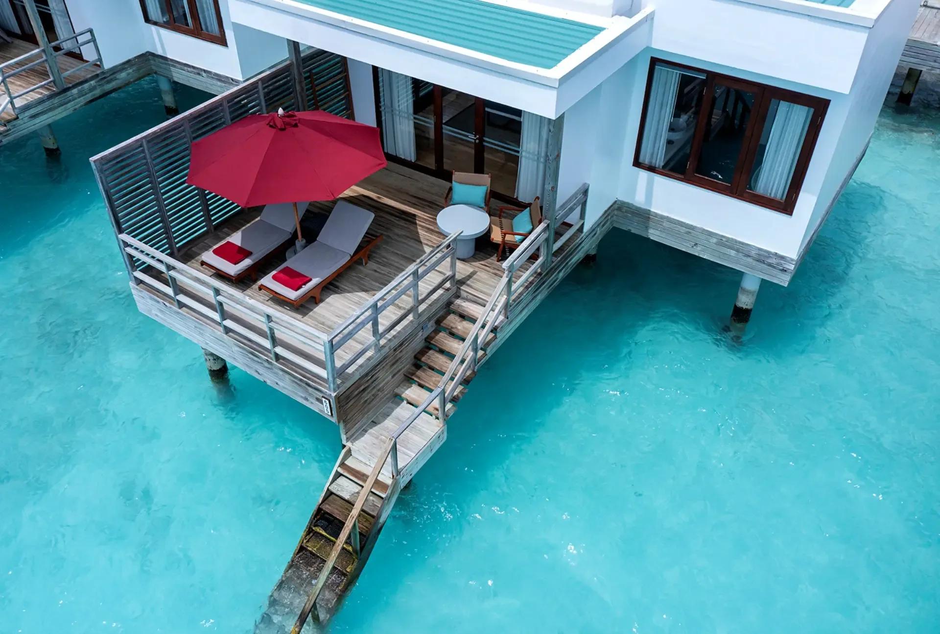 Aerial view of a Water Villa's overwater deck and open-air lounge chairs above the turquoise lagoon