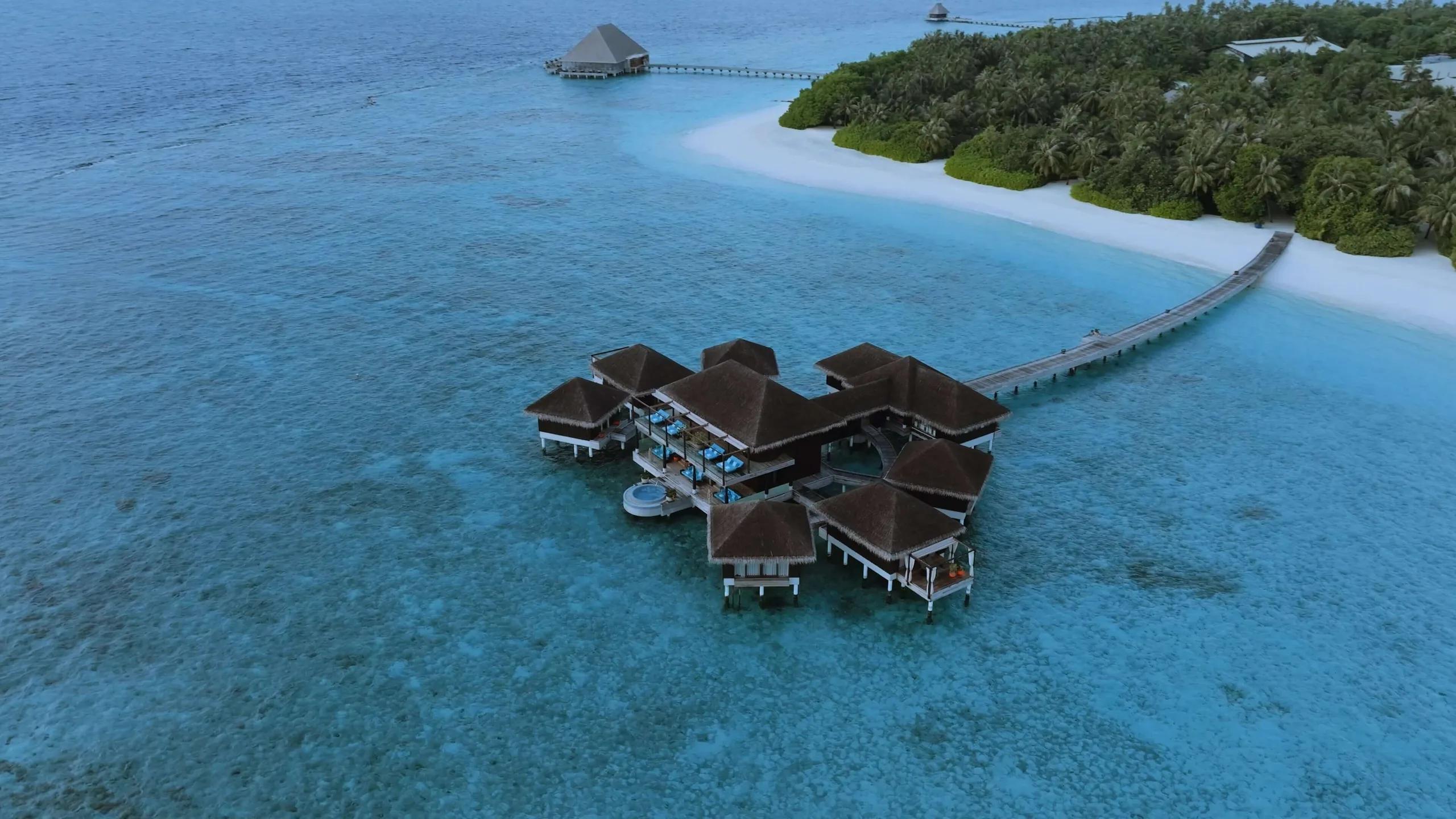 An aerial view of Velaa's overwater spa pavilions, connected to the main island by a long wooden walkway