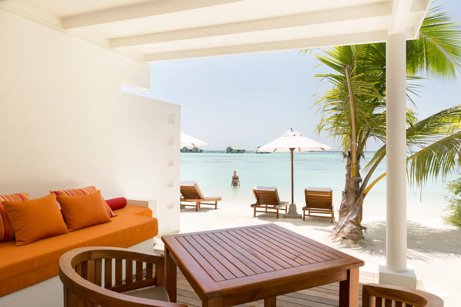 A Family Lagoon Pavilion's terrace with orange-cushioned daybeds, looking across the lagoon to the overwater villa row