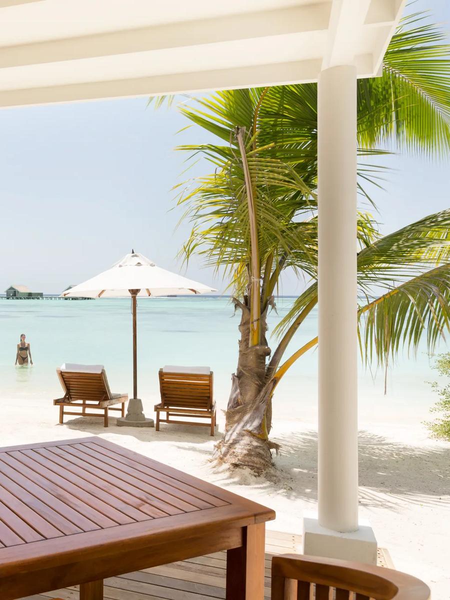 A Family Lagoon Pavilion's terrace with orange-cushioned daybeds, looking across the lagoon to the overwater villa row