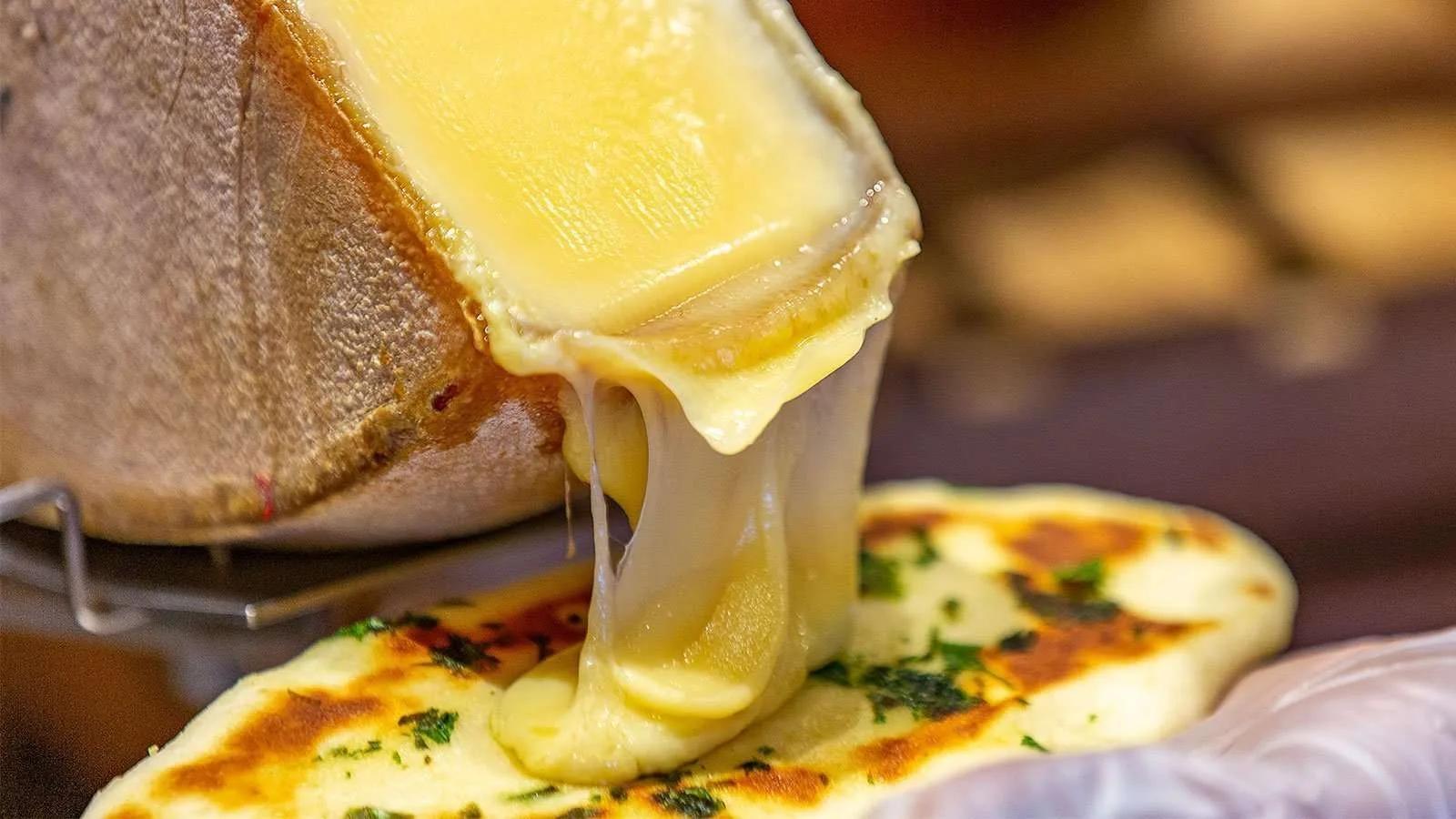 Melted cheese pulled from a raclette wheel over a herb flatbread, a dish served at Junk Food Kitchen