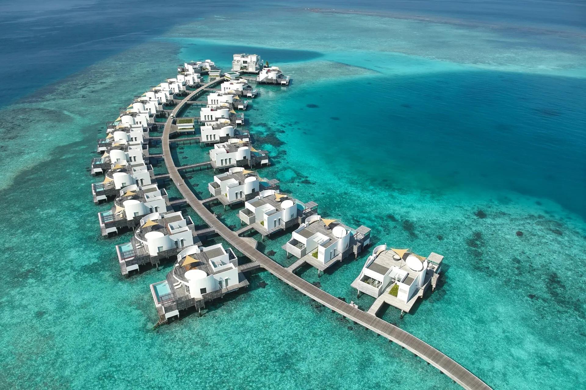 Aerial view of Jumeirah Olhahali's overwater One Bedroom Water Villas, arranged along a boardwalk over the reef in North Malé Atoll