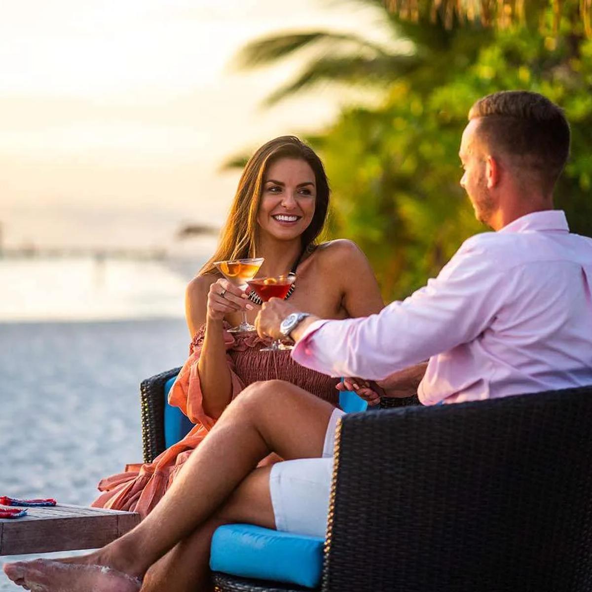 A couple sharing cocktails at Thundi Bar as the sun sets over the lagoon behind them