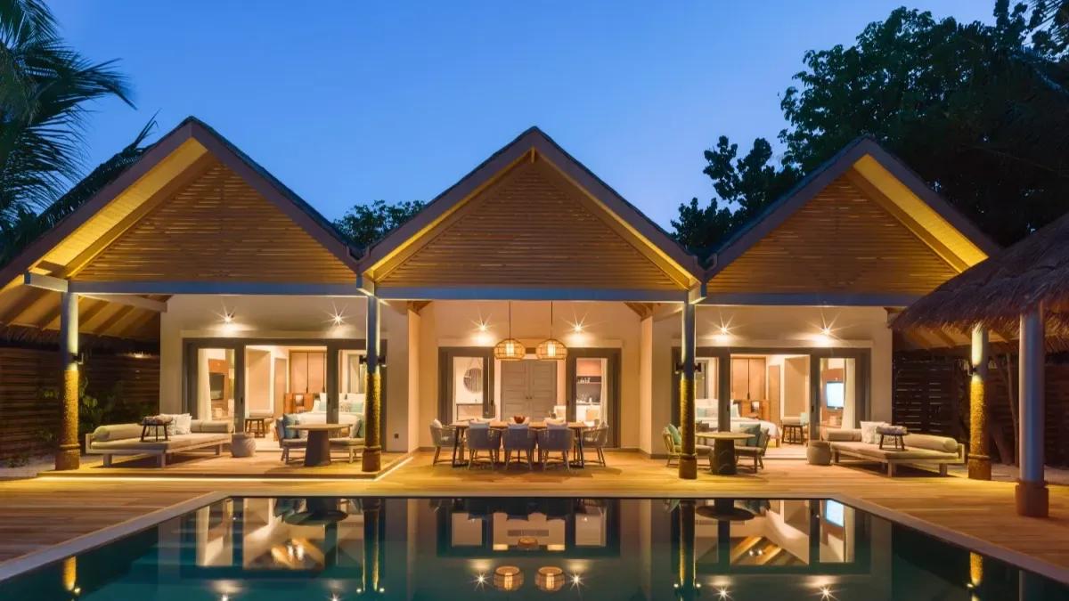 The Four Bedroom Beach Pool Residence's three thatched pavilions lit at night, reflected in its private pool
