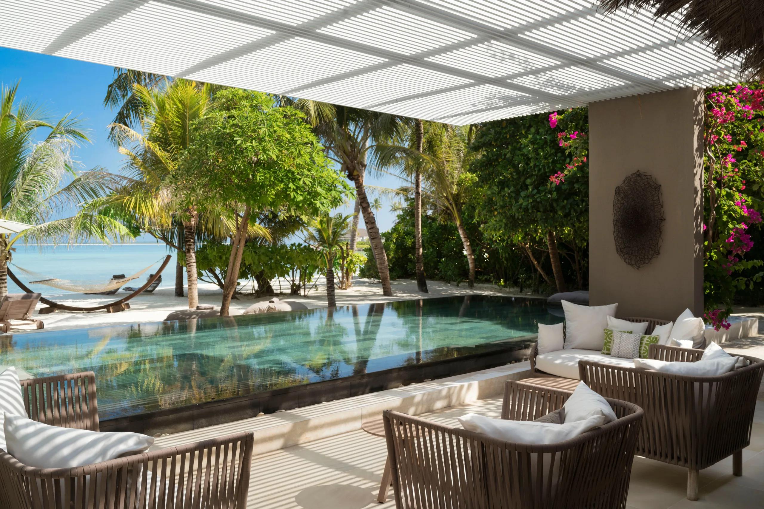 An Island Villa's infinity pool deck with a hammock and daybeds looking out past palm trees to the ocean