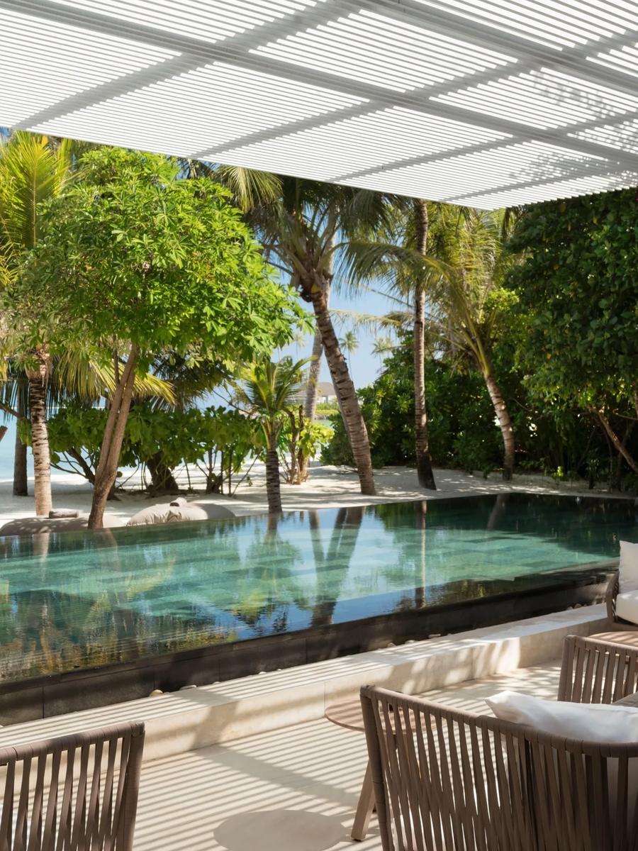 An Island Villa's infinity pool deck with a hammock and daybeds looking out past palm trees to the ocean