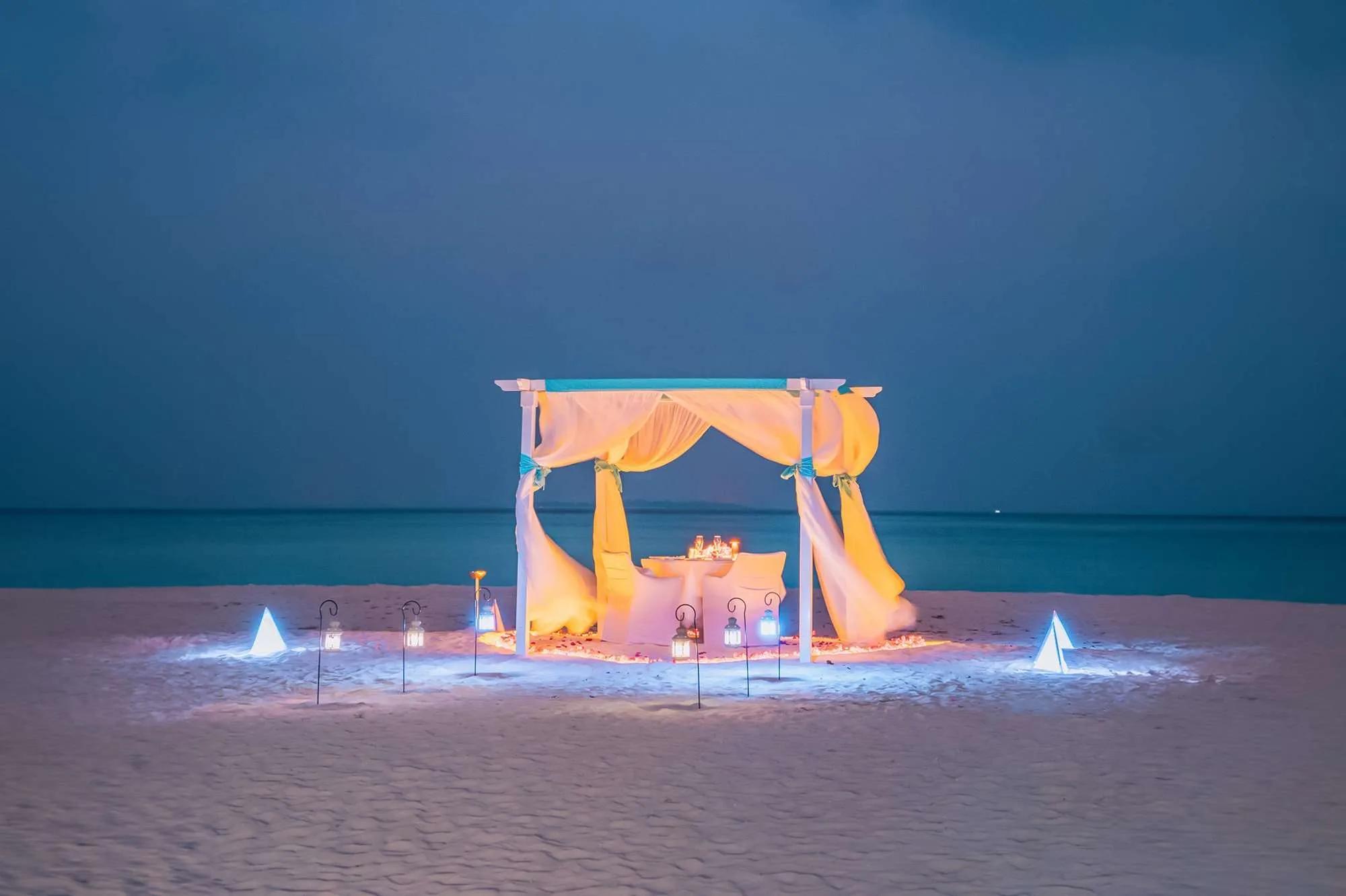 A private beach dinner setup lit by lanterns at night, Hideaway Beach Resort & Spa