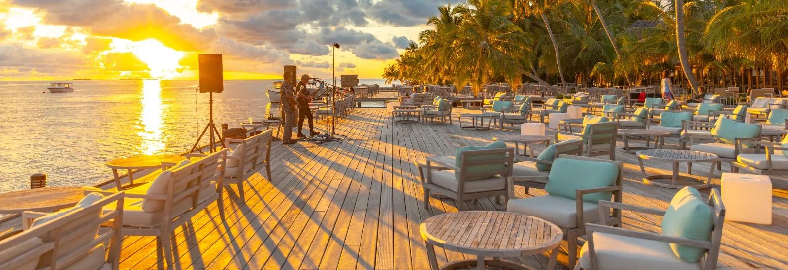 Musicians performing at sunset on Bonthi Bar's overwater deck, with loungers set out for guests