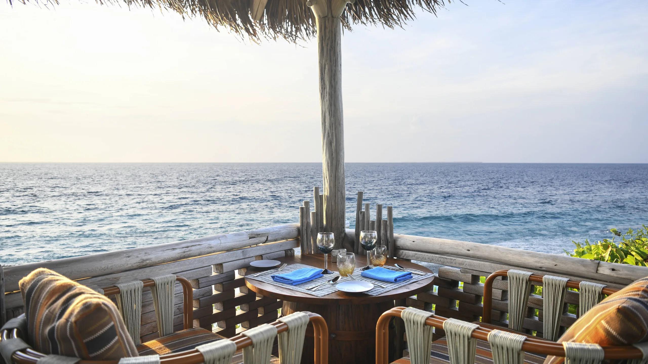 A table set for two at Kaashi, under a thatched roof looking straight out over open water