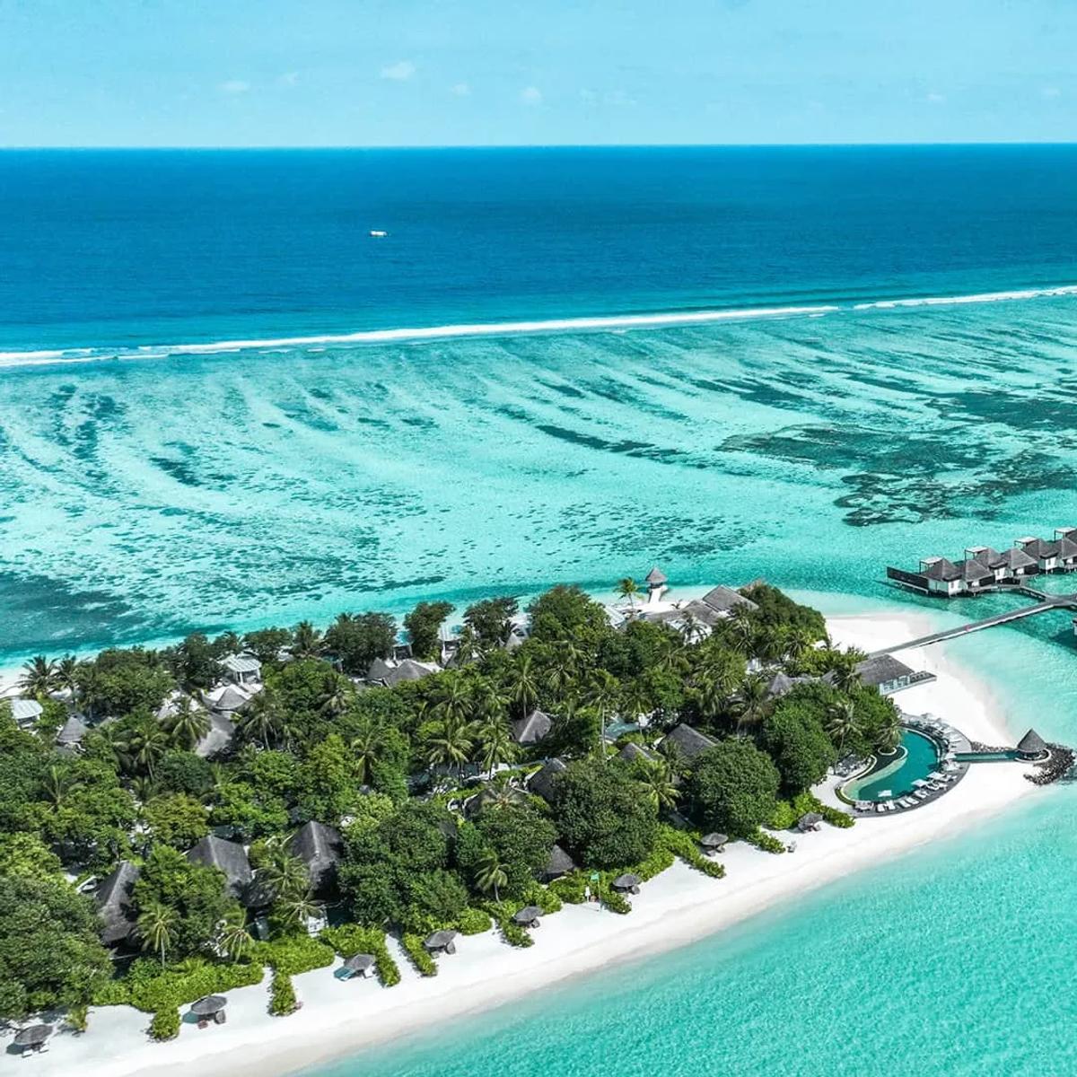 Aerial view of Four Seasons Resort Maldives at Kuda Huraa, its overwater villas running out along the reef edge in North Malé Atoll