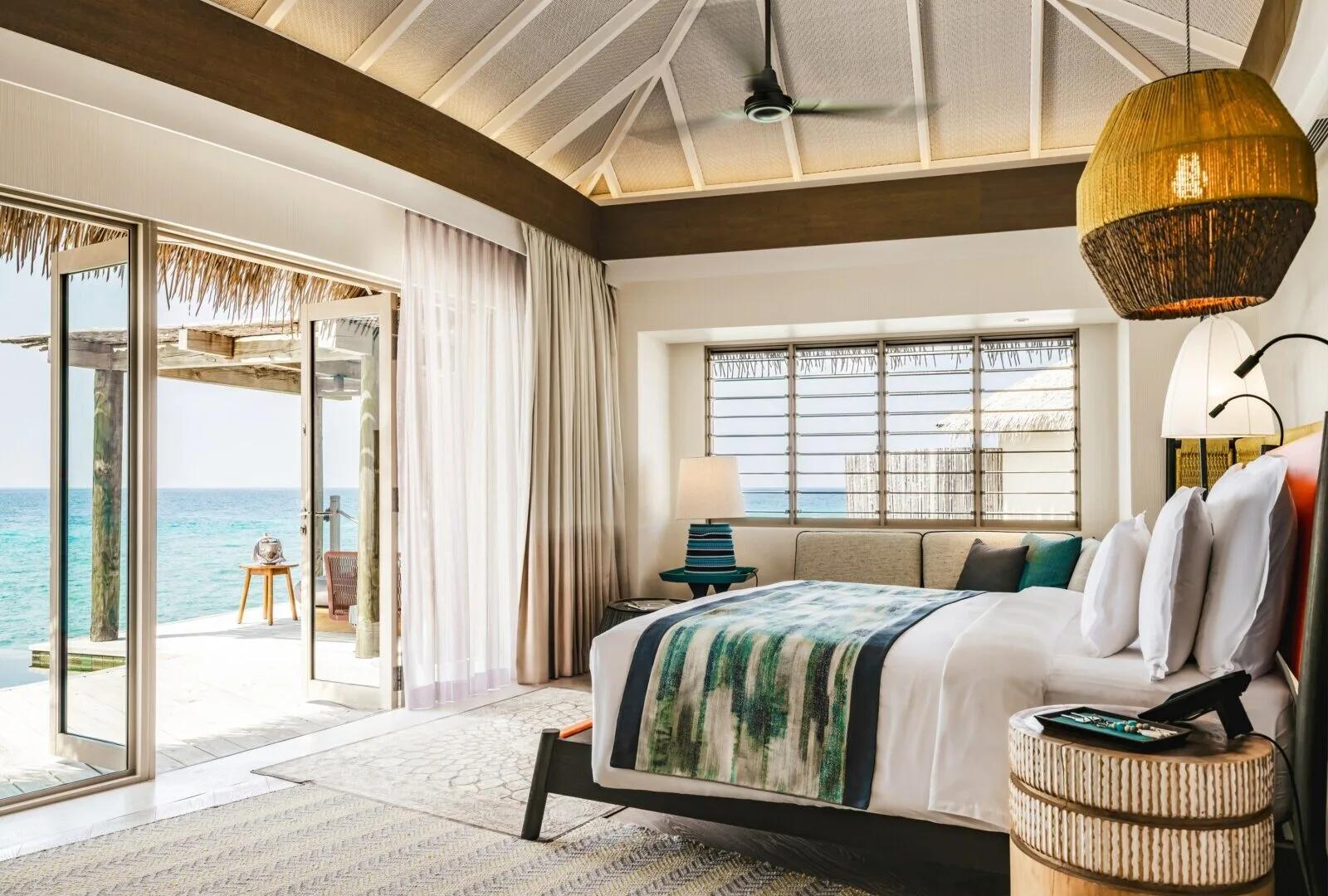 The bedroom of an Overwater Pool Villa, glass doors open to a private deck over the lagoon