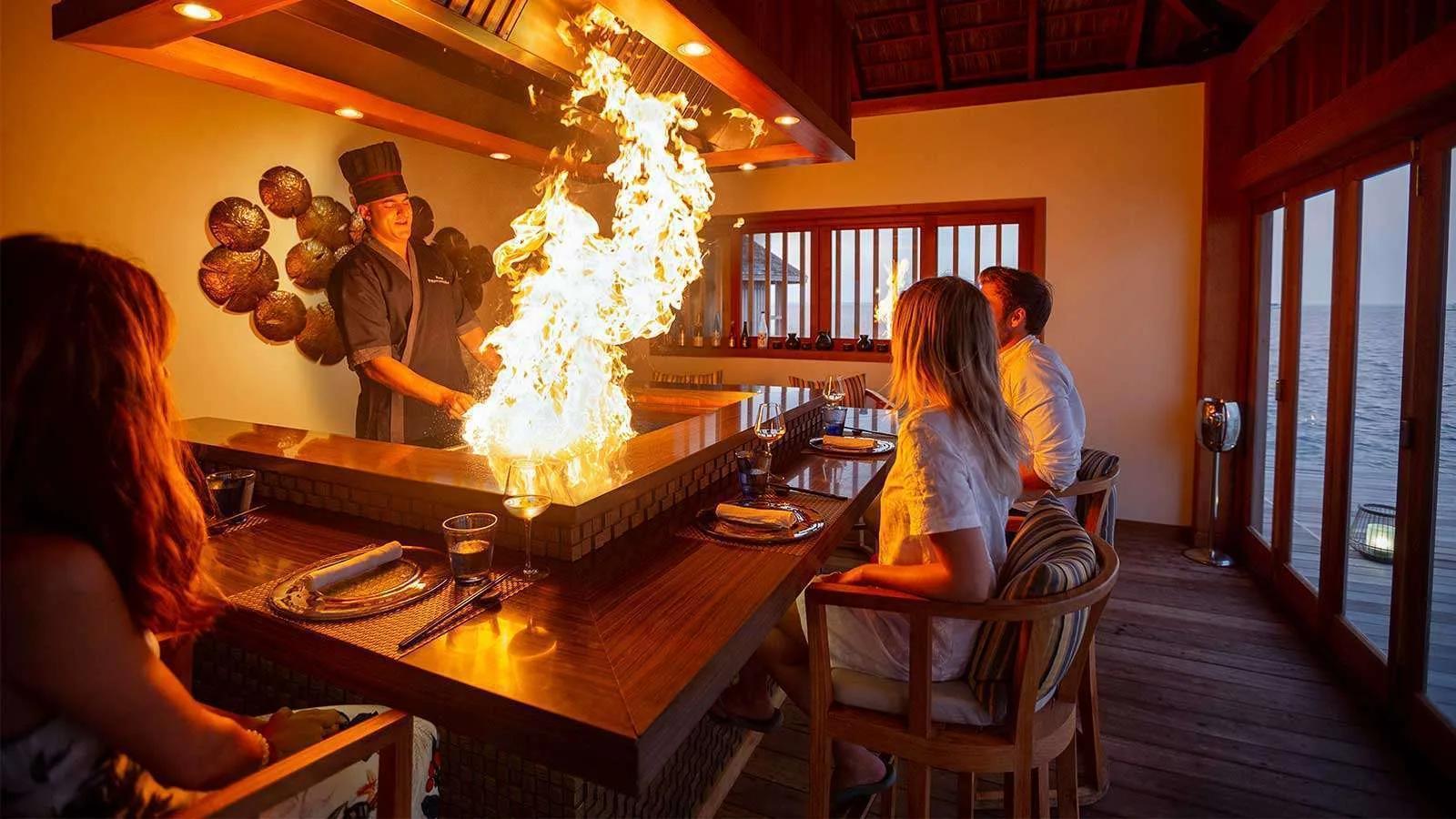 A chef sends flame up from the teppanyaki grill at Kashibo's counter, guests watching from their seats
