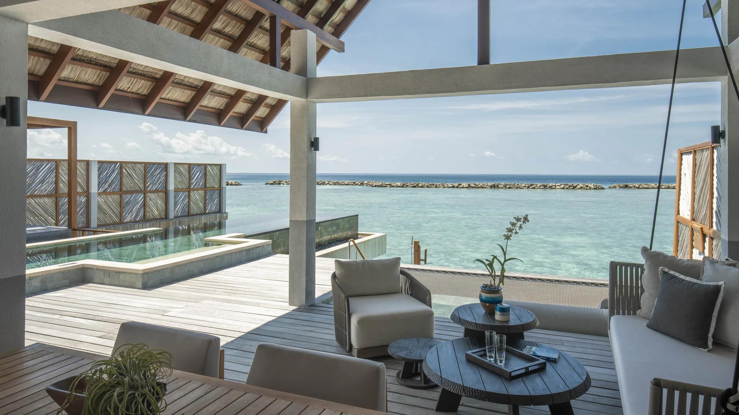 The overwater deck and plunge pool of a Sunrise Family Water Villa, loungers set out with the reef breakwater visible beyond