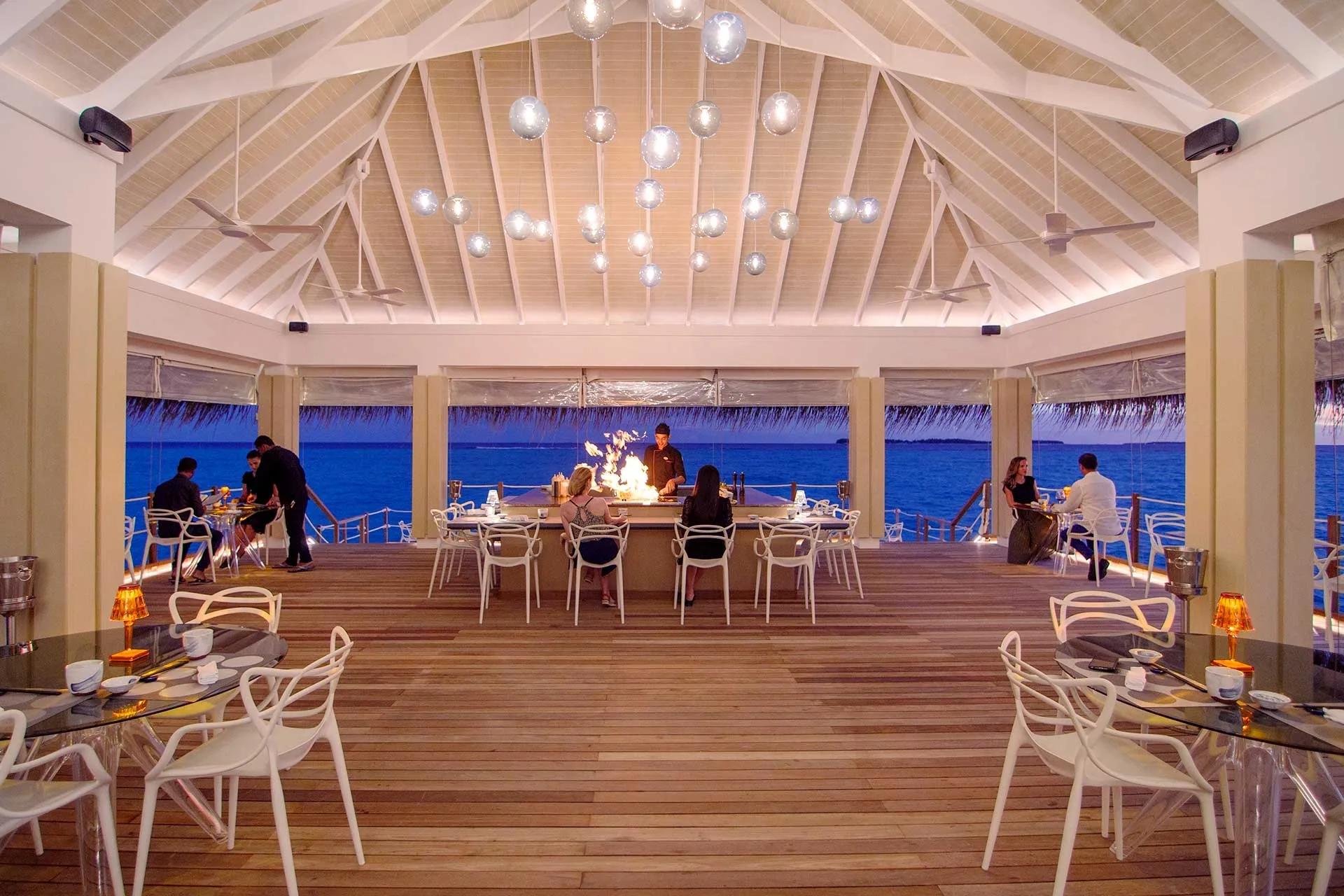 Guests seated at Yama's glass-topped tables as the open teppanyaki bar behind them catches flame at dusk