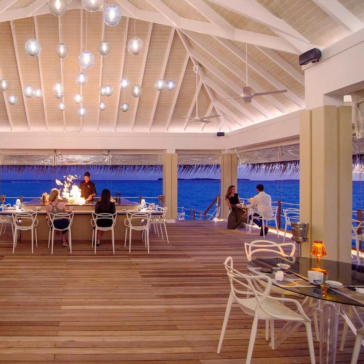 Guests seated at Yama's glass-topped tables as the open teppanyaki bar behind them catches flame at dusk