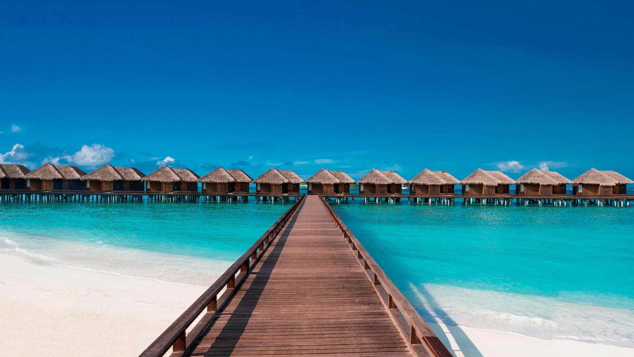 A long wooden jetty leading from the beach to a row of thatched-roof overwater villas