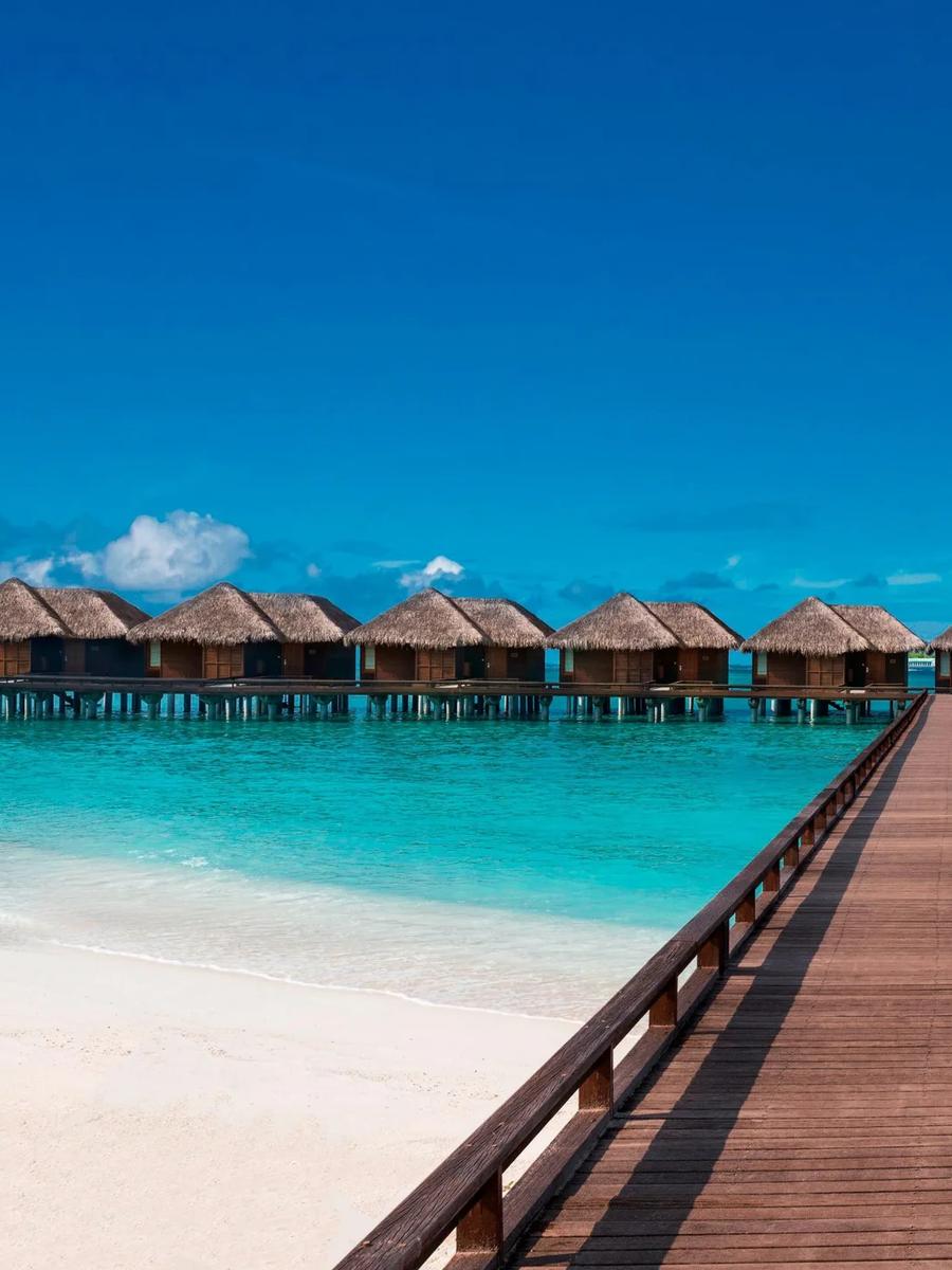 A long wooden jetty leading from the beach to a row of thatched-roof overwater villas