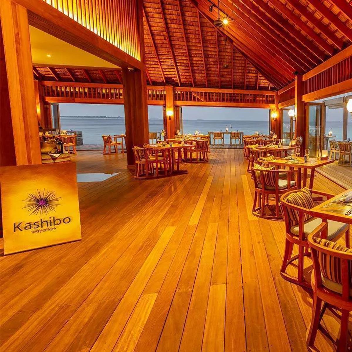 Kashibo's overwater dining room at dusk, tables set along glass walls facing the lagoon