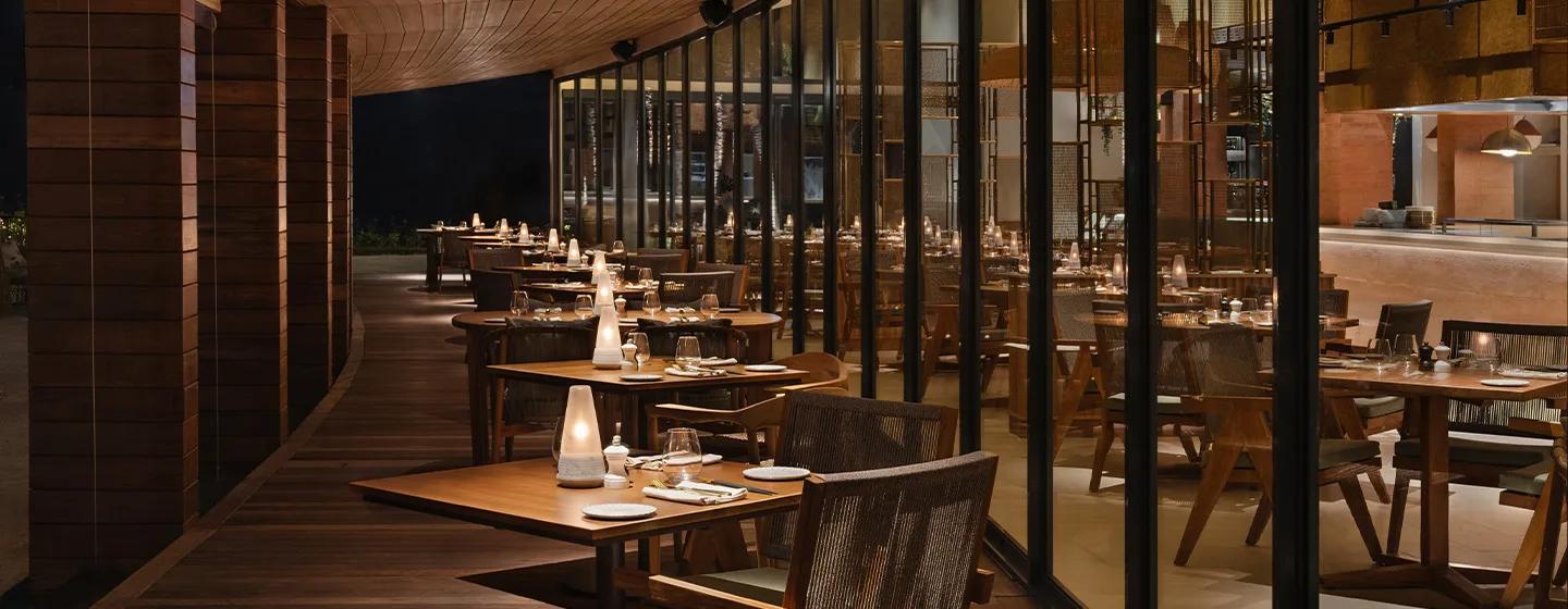 The Citronelle Club's beachfront dining room at SO/ Maldives, tables lit for dinner beside an open, glass-walled exhibition kitchen