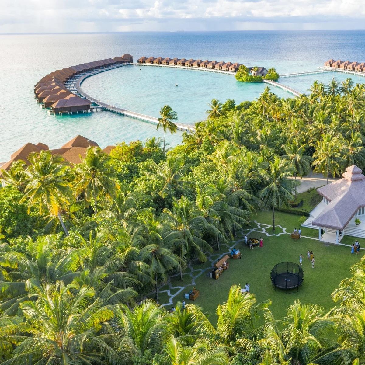 Aerial view of Ayada Maldives — the horseshoe of overwater villas enclosing a shallow lagoon, with the garden and lawn pavilion in the foreground