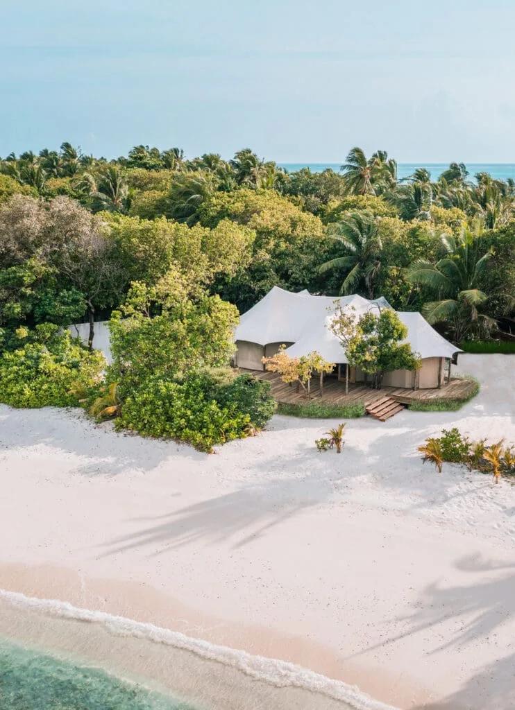 Aerial view of a Safari Tented villa's canvas roofline set among jungle trees just behind the beach