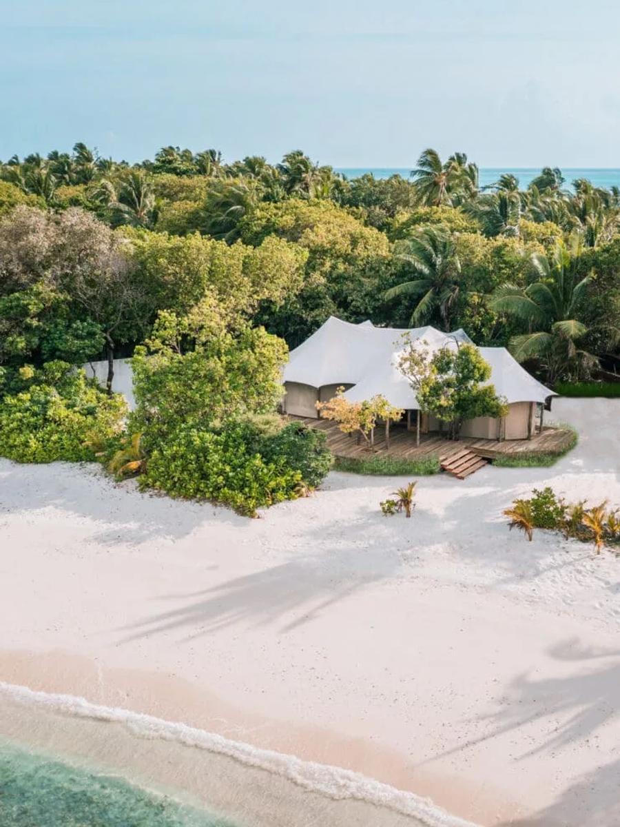 Aerial view of a Safari Tented villa's canvas roofline set among jungle trees just behind the beach