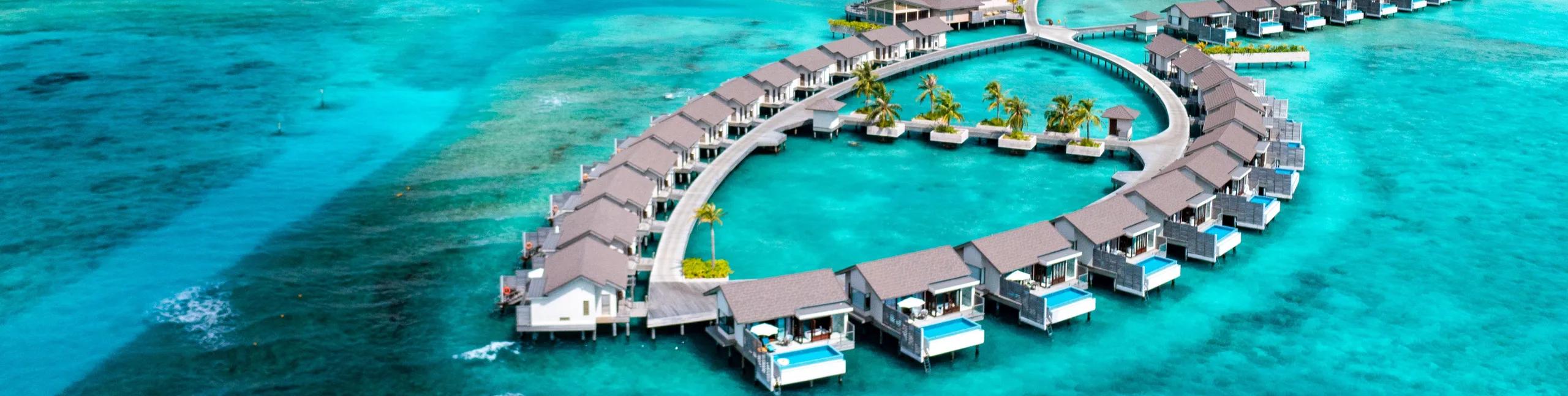 An aerial view of Atmosphere Kanifushi Maldives' ring of overwater villas reaching into the turquoise lagoon