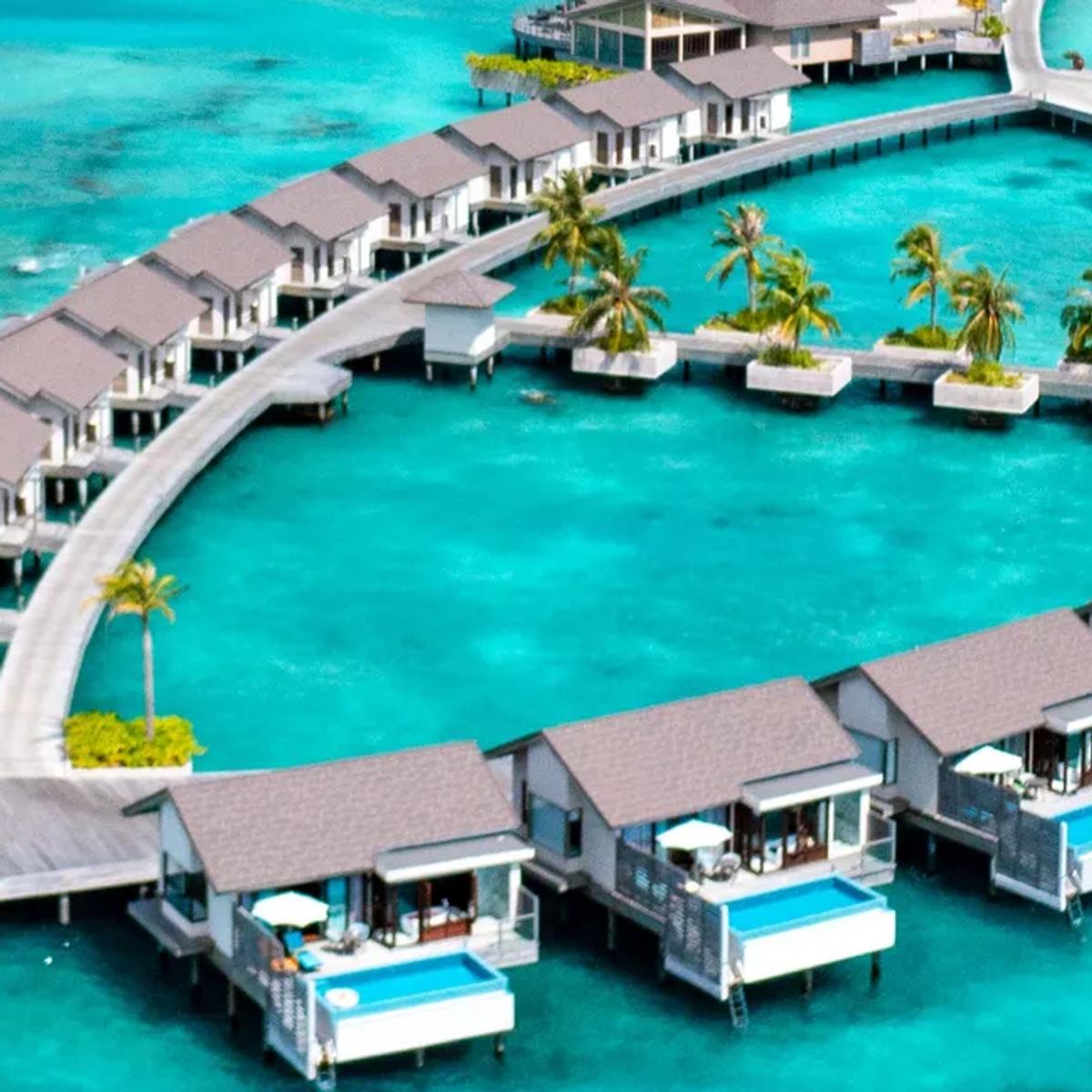 An aerial view of Atmosphere Kanifushi Maldives' ring of overwater villas reaching into the turquoise lagoon