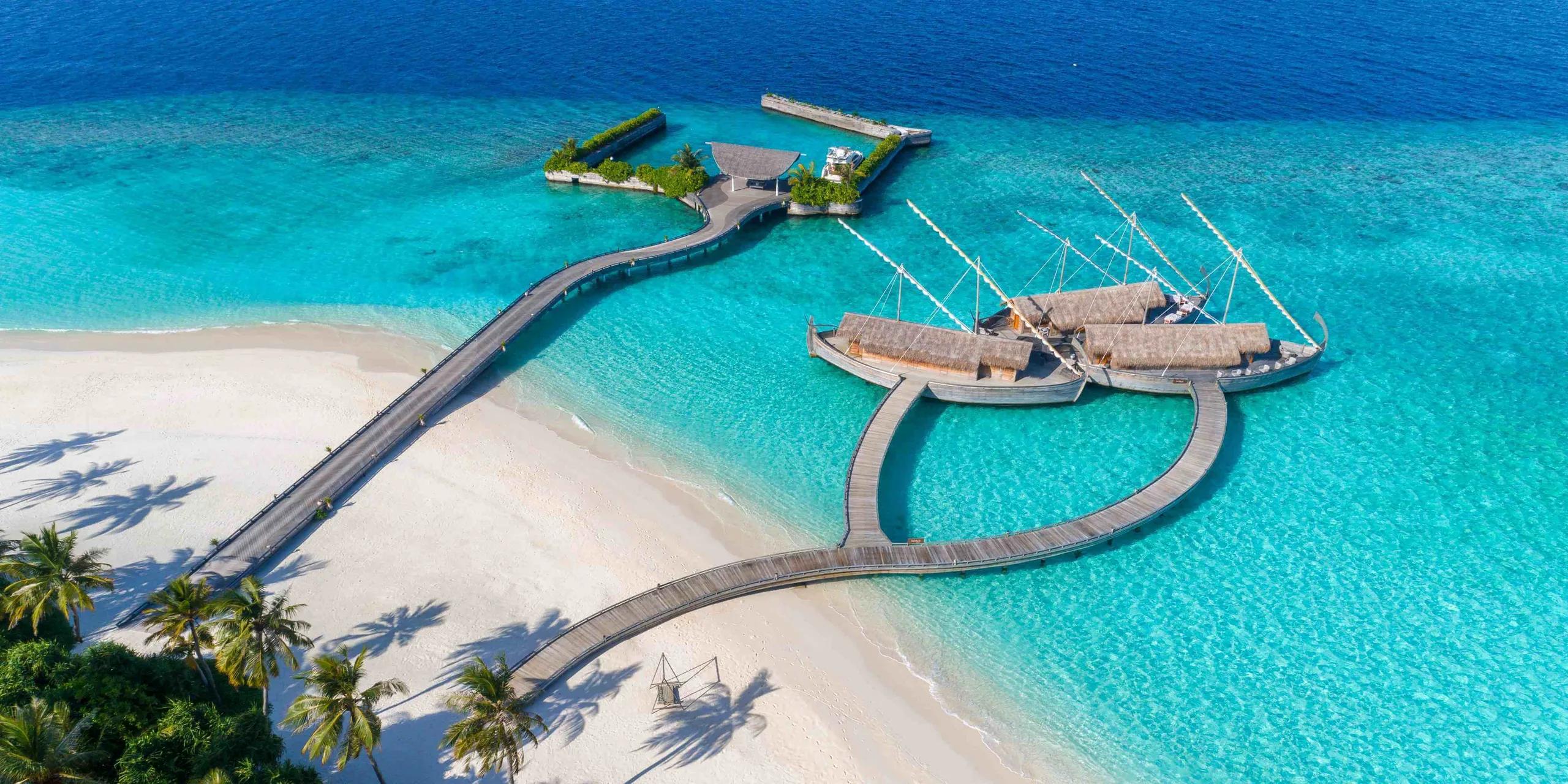 Aerial view of Ba'theli by the Reef, Milaidhoo's overwater restaurant, its three boat-shaped pavilions and boardwalk reaching out from the beach into the lagoon.