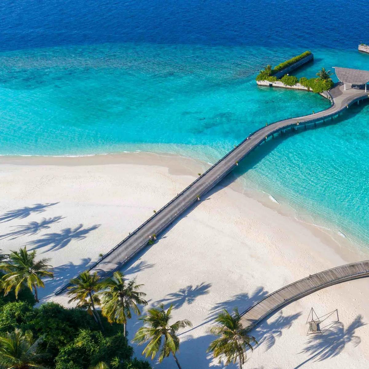Aerial view of Ba'theli by the Reef, Milaidhoo's overwater restaurant, its three boat-shaped pavilions and boardwalk reaching out from the beach into the lagoon.