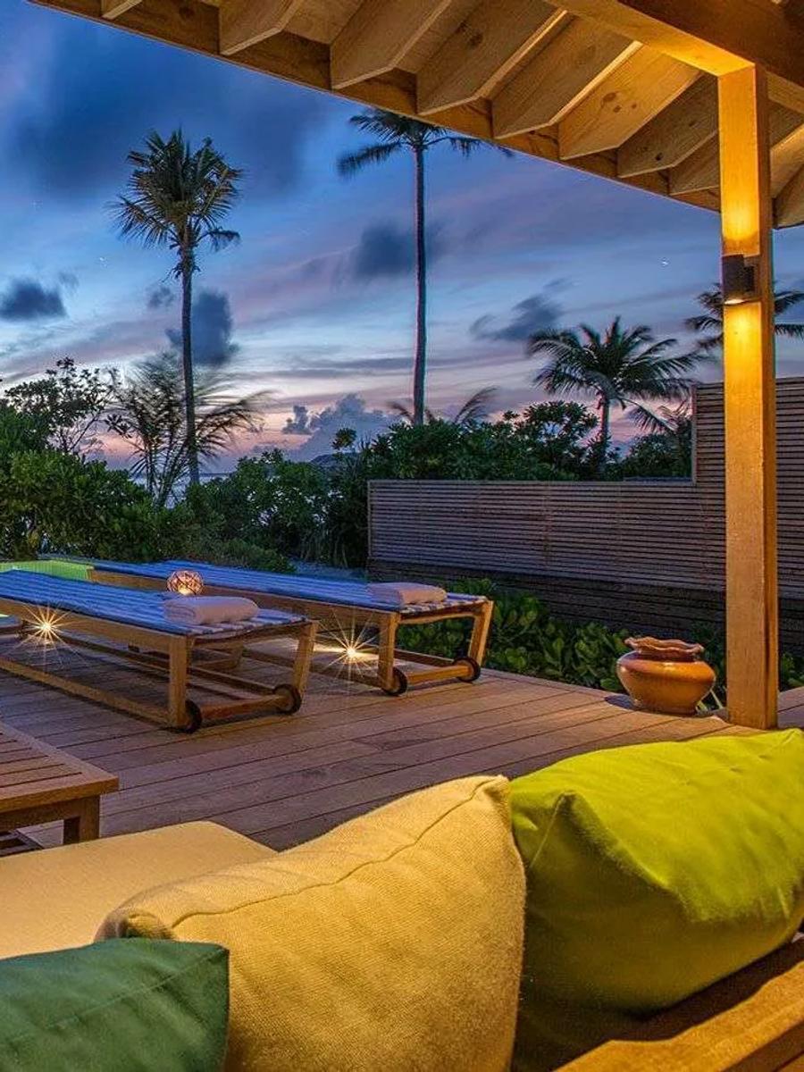 A Beach Sunset Pool Villa's infinity pool and deck lounge at dusk, palm trees silhouetted against the fading sky