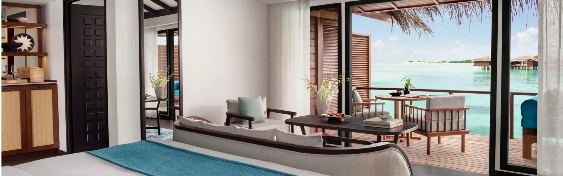 Over Water Villa living area opening onto a lagoon-facing deck under a thatch roof