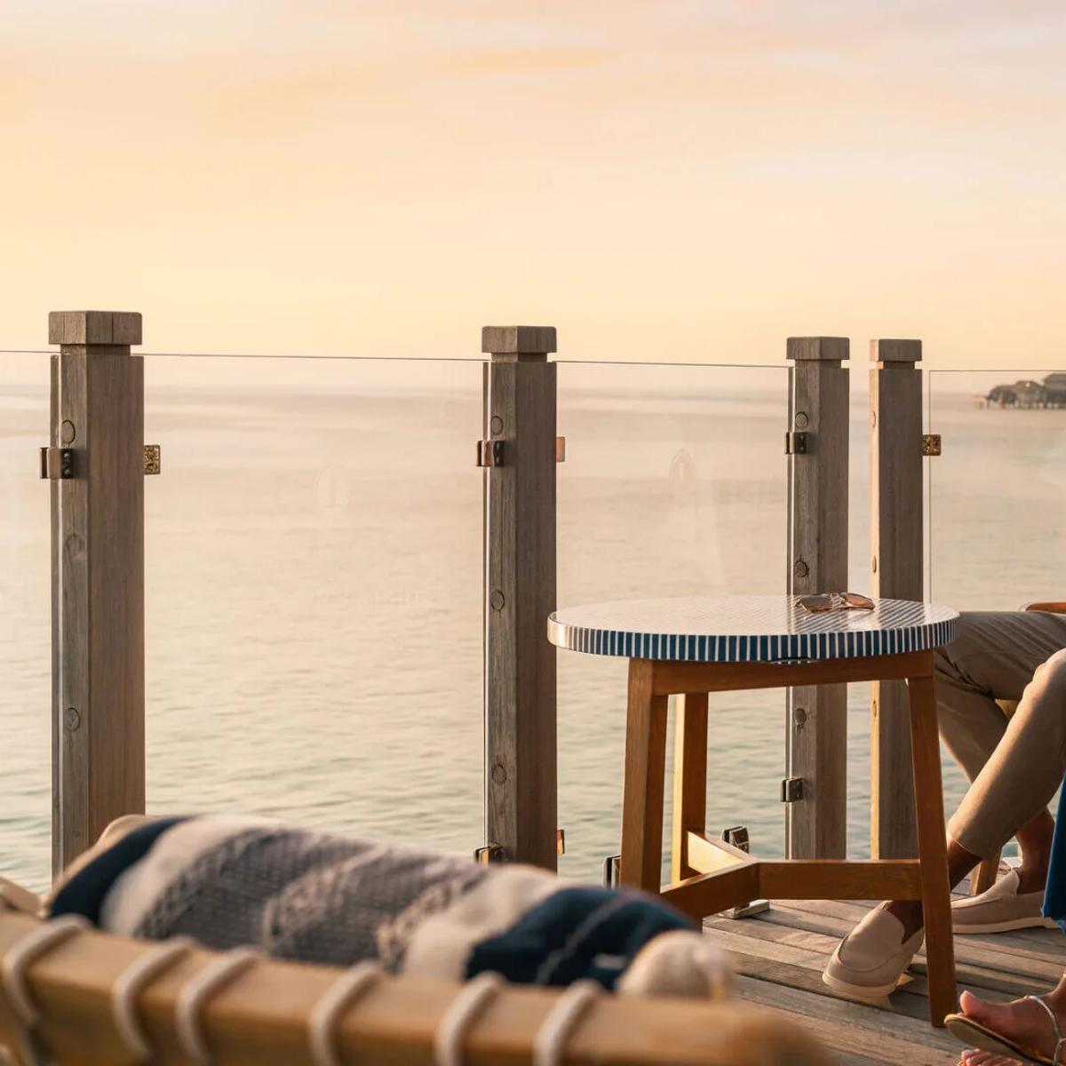 A couple sharing champagne on an overwater deck at sunset, with villas lined up behind them