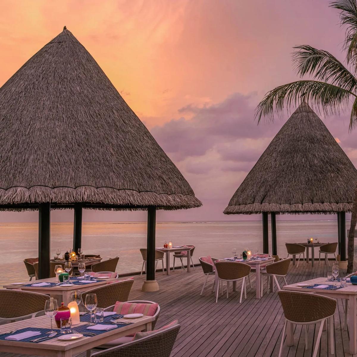 Kandu Grill's thatched pavilions lit at dusk, tables set beside the pool and lagoon